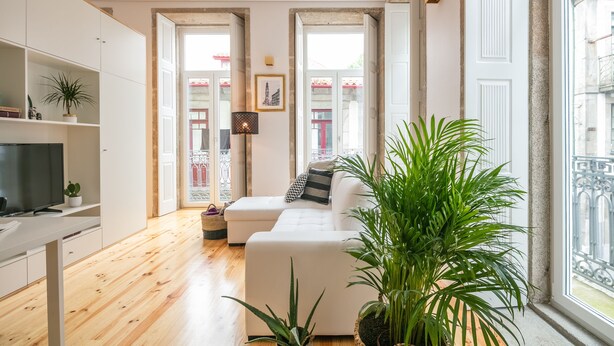 A modern living room with a white sofa, wooden flooring, and a large window offering a view of the outside. - Indulge Porto Flats (Porto)