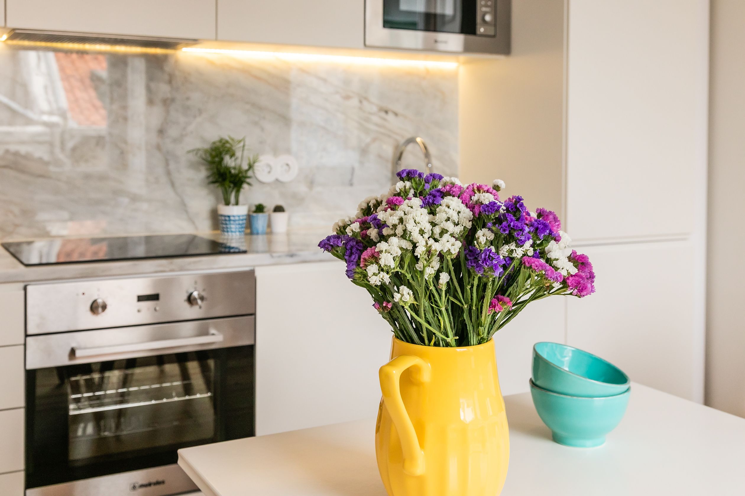 Eine Küche mit einem gelben Blumenstrauß in einer Vase, einer blaugrünen Schüssel und modernen Geräten.