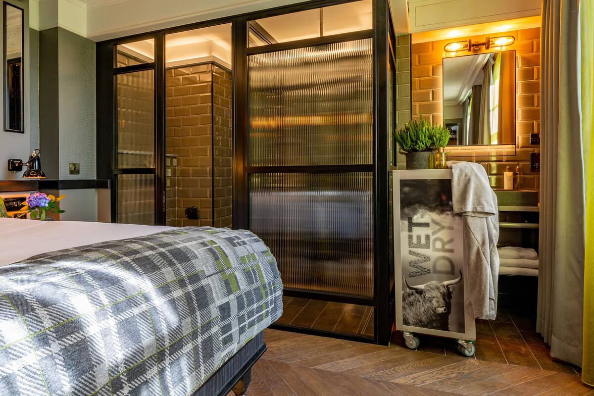 Une chambre d’hôtel avec un lit, une porte coulissante, une salle de bain avec un miroir et un chariot avec une serviette.