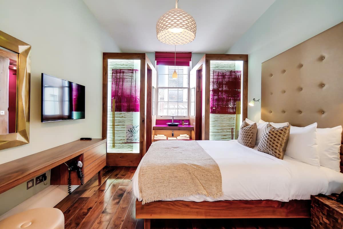 Une chambre moderne avec un grand lit, un plancher en bois, une télévision, un bureau et un luminaire au plafond original.