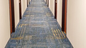 A long, narrow hotel corridor with patterned carpet, doors on both sides, and a bright overhead light. - American Inn and Suites Ferndale (Ferndale)