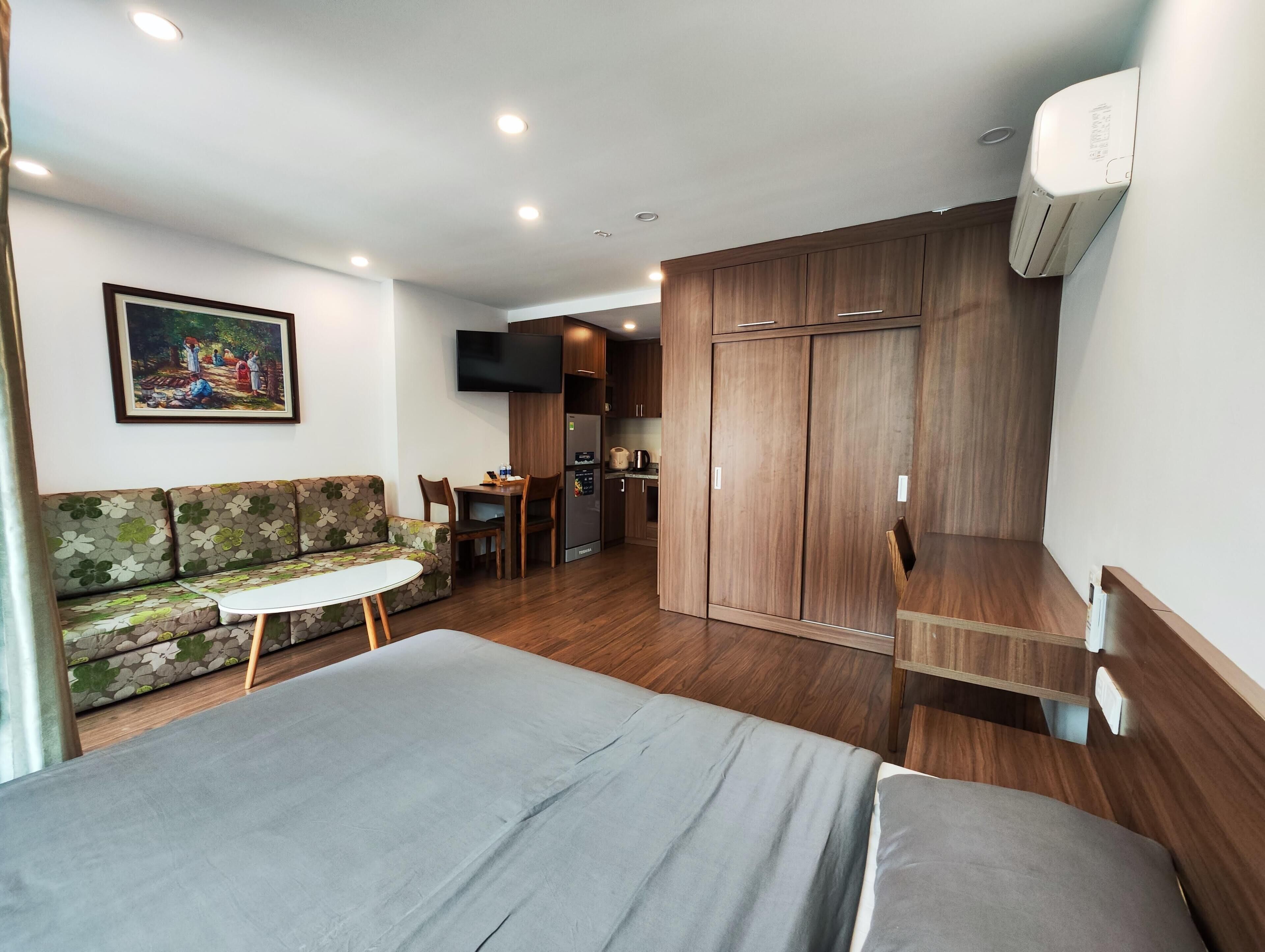 A modern hotel room with a bed, sofa, dining table, and kitchenette.