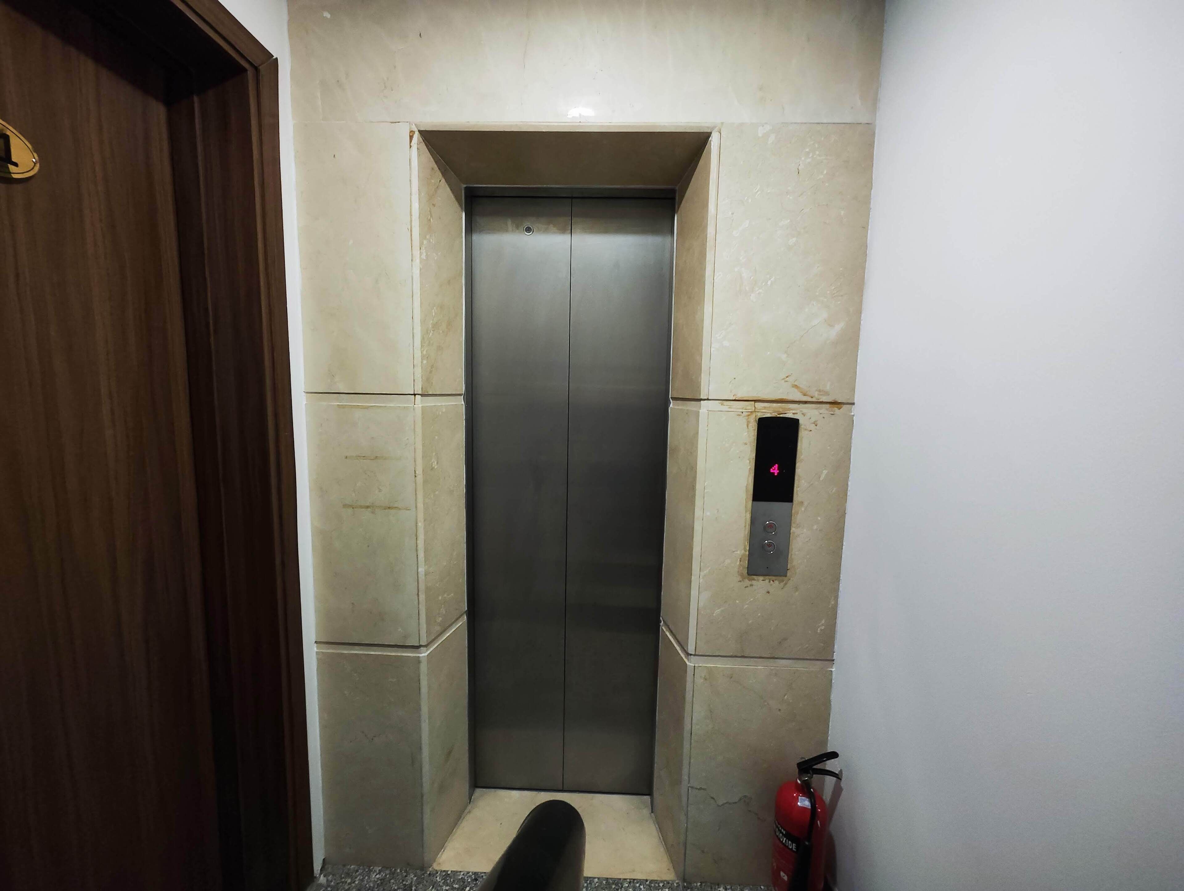 Un ascensor con una pantalla digital que muestra el número 4, un extintor de incendios montado en la pared y una puerta de madera a la izquierda.