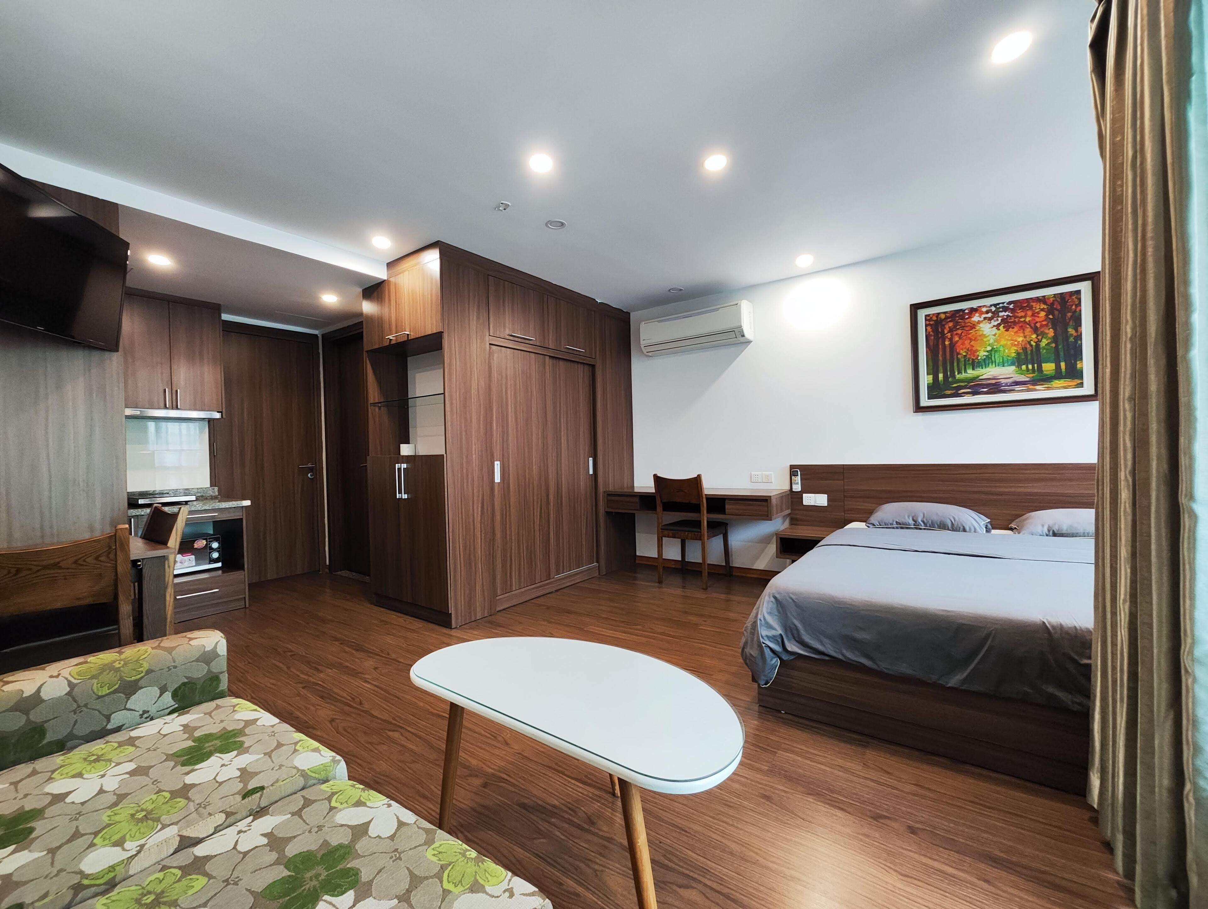 A compact hotel room with a kitchenette, a bed, a small table, and a sofa.