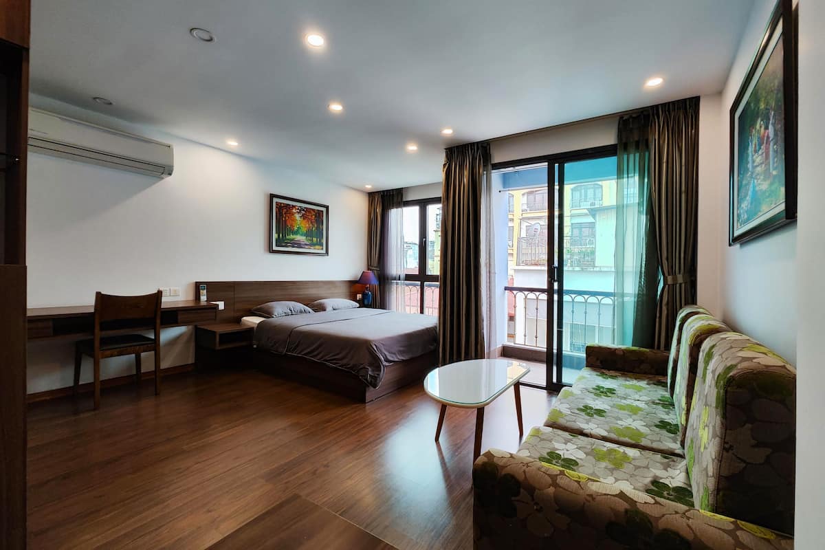 Quarto de hotel moderno com cama, escrivaninha, cadeira, sofá e uma varanda com cortinas.