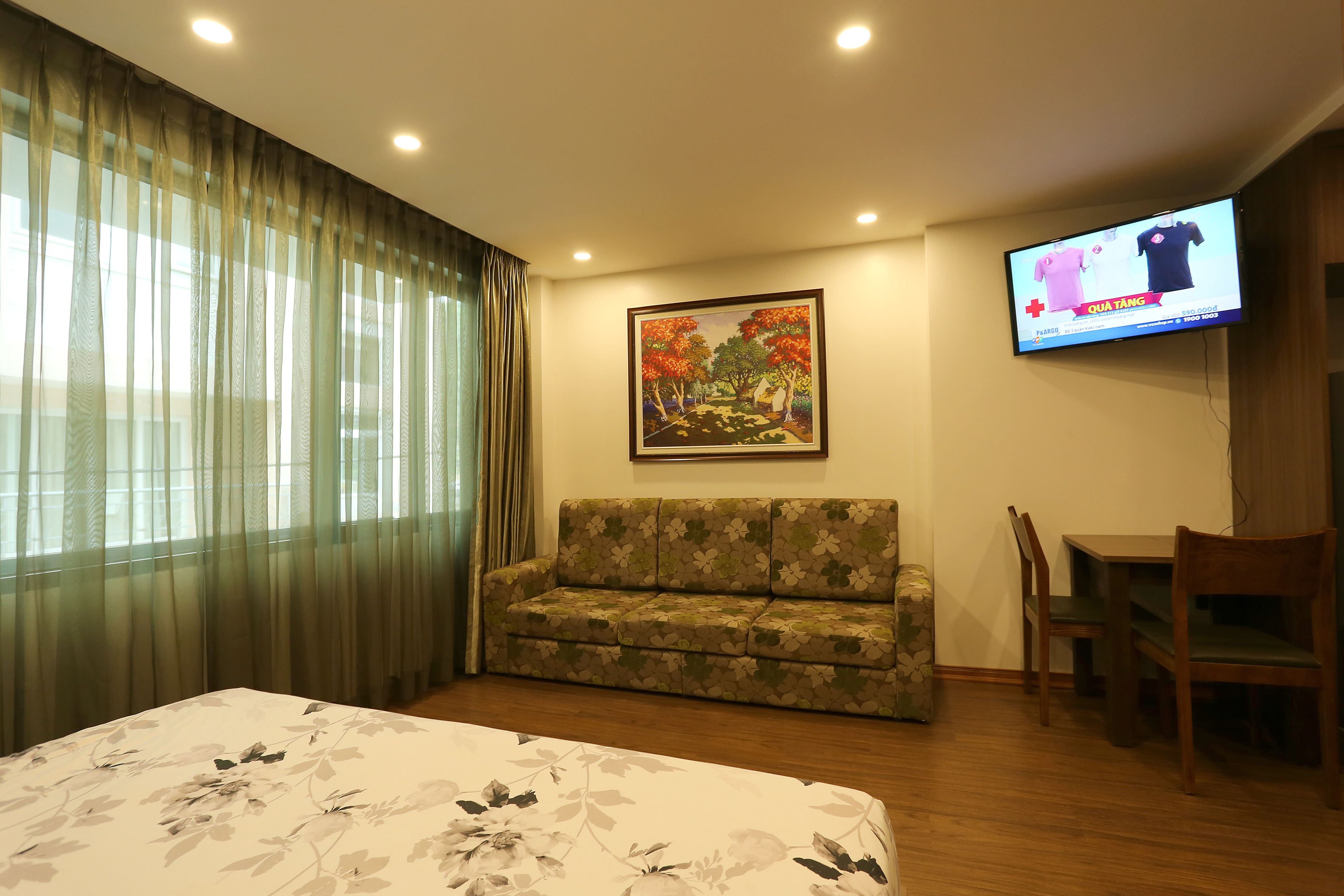 Habitación de hotel con cama, sofá, televisor y un cuadro en la pared.