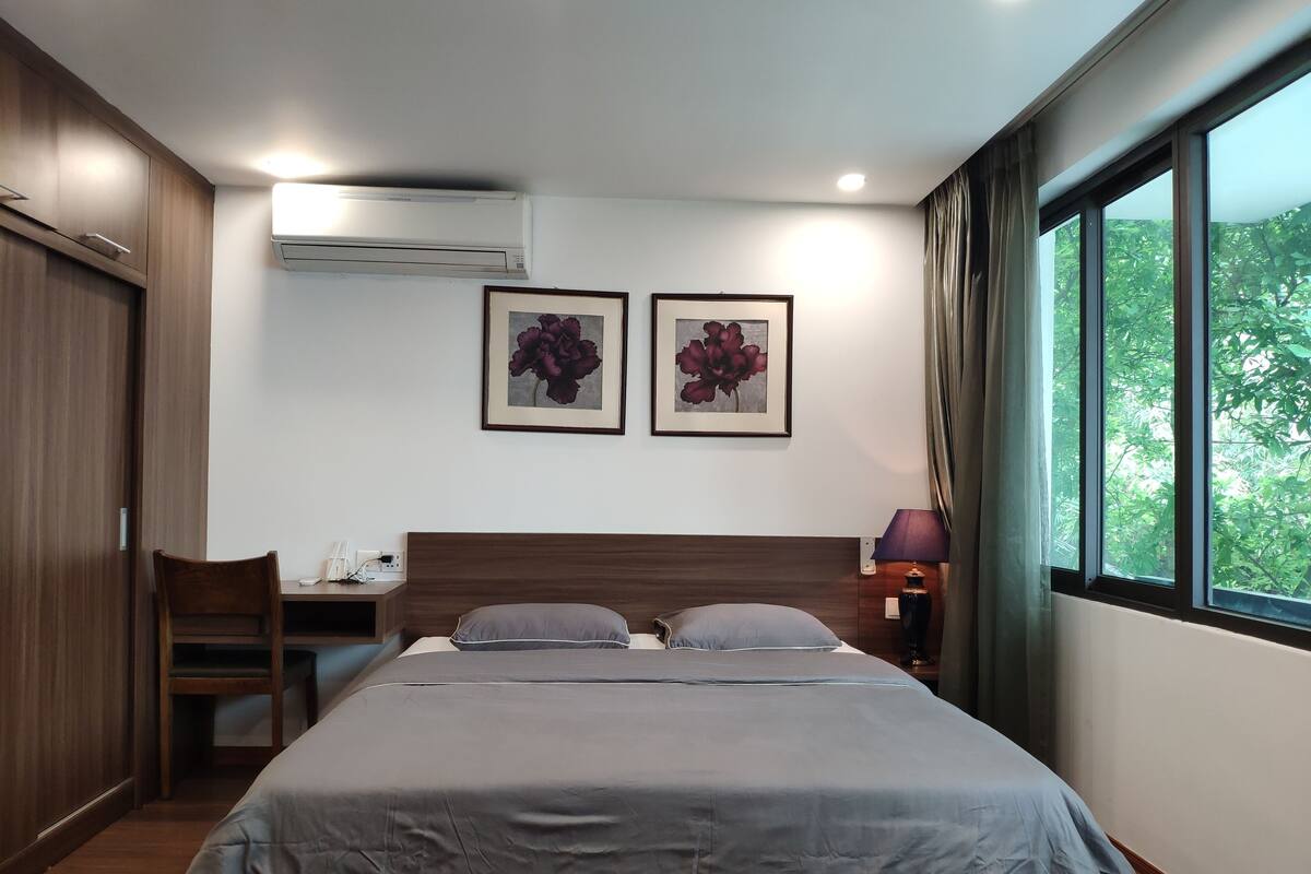 Quarto de hotel com cama, escrivaninha, ar condicionado e duas fotos emolduradas na parede.
