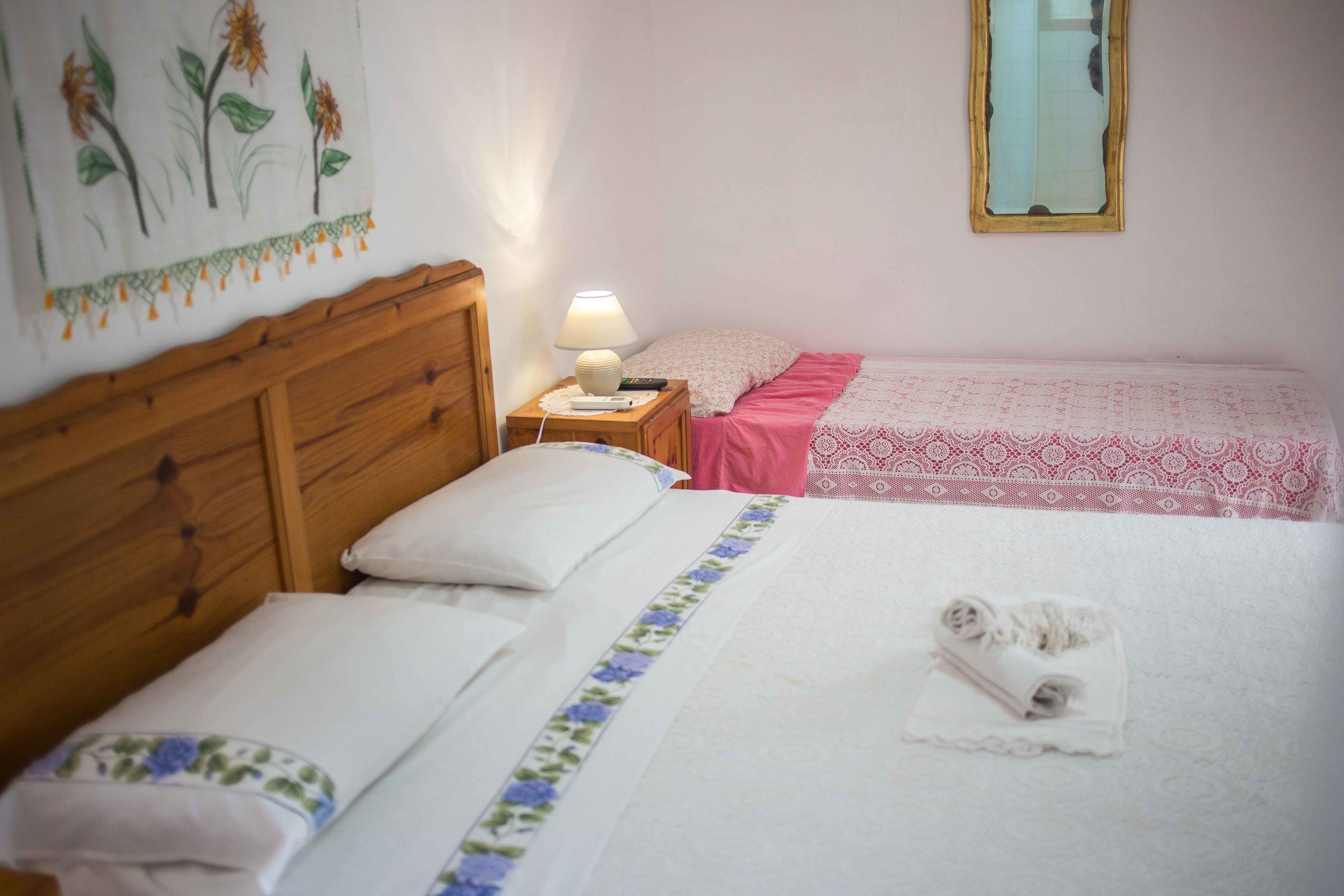 Camera d'albergo con due letti, una testiera in legno, un comodino con una lampada, uno specchio e un arazzo floreale sulla parete.