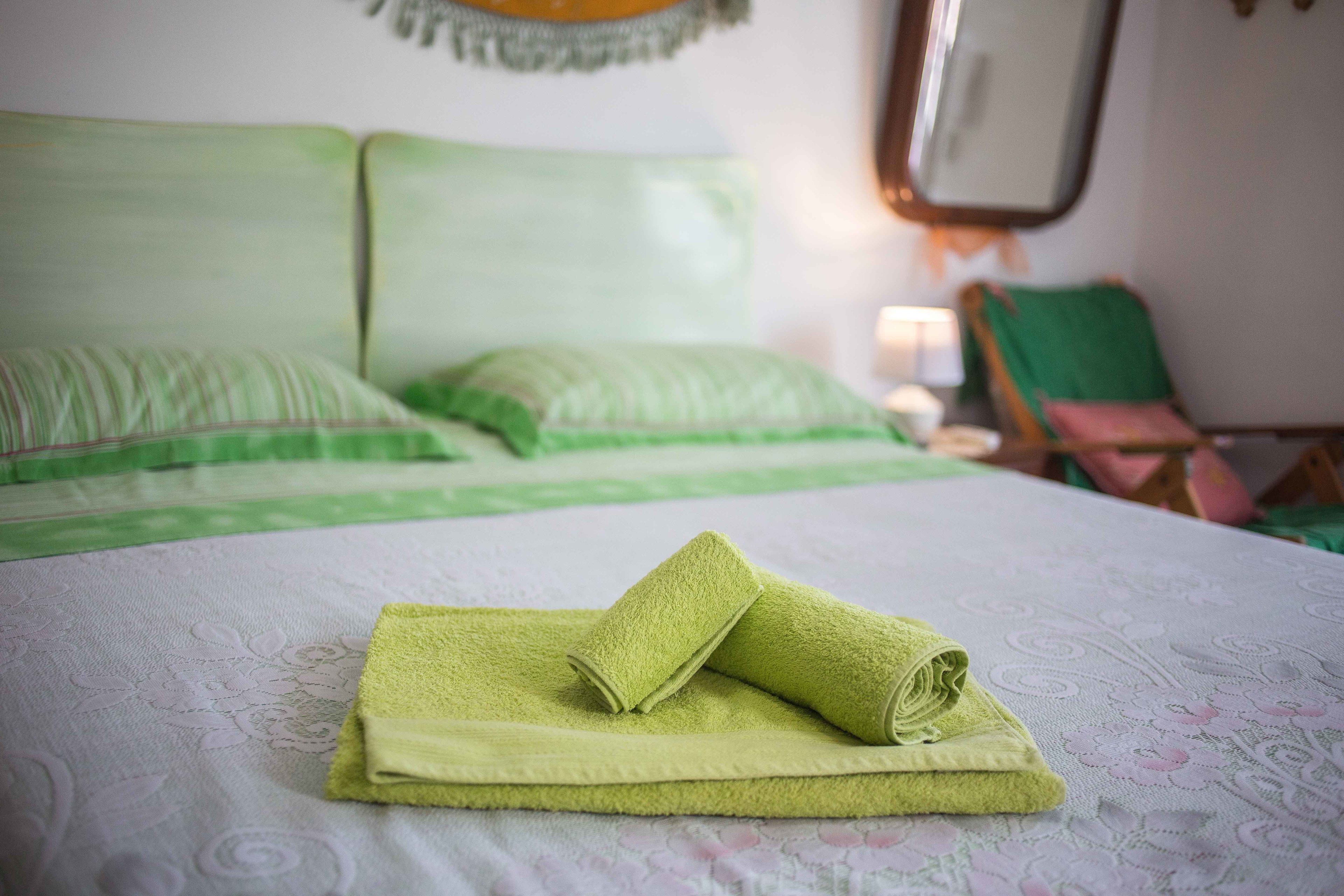 Un letto rifatto con cura, asciugamani verdi, una testiera verde e una sedia verde in una stanza con una coperta a motivi.