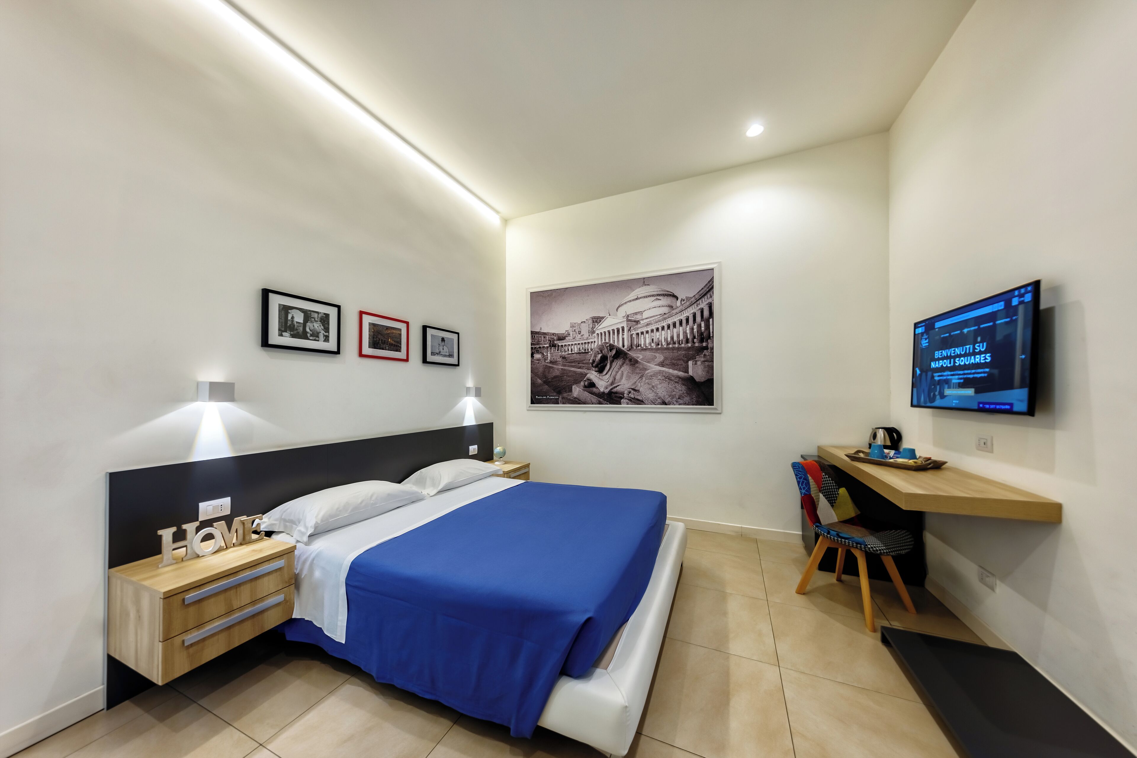 Een moderne hotelkamer met een bed, nachtkastjes, een bureau met stoel, een flatscreen televisie en kunstwerken aan de muur.