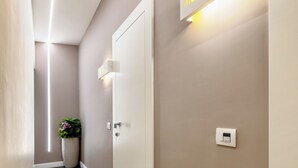 A hallway with a modern design, featuring a light fixture with the name "nicola more" and a thermostat on the wall. - Napoli Squares Suites (Naples)