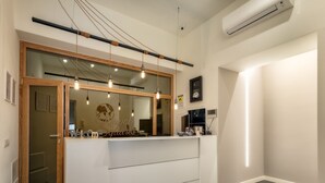 A reception desk with a wooden frame and a large mirror, a clock, and a small TV on the wall. - Napoli Squares Suites (Naples)