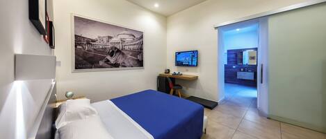 A hotel room with a bed, a desk with a computer, a television, and a large wall picture.