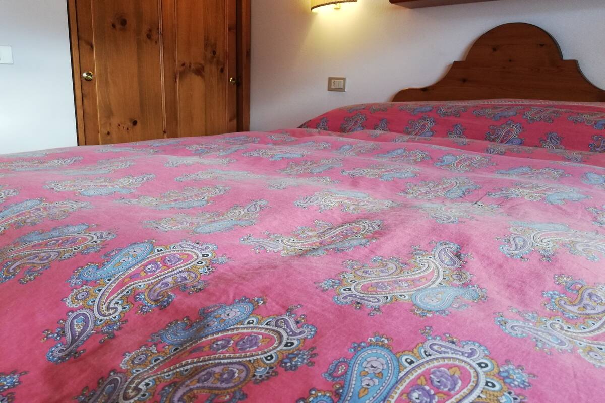 A bedroom with a wooden headboard, a pink patterned bedspread, and a wall-mounted lamp.