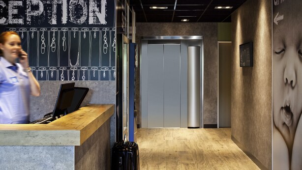 Una mesa de recepción con una pizarra que muestra los números de las habitaciones, una encimera de madera y un teléfono instalado en la pared.