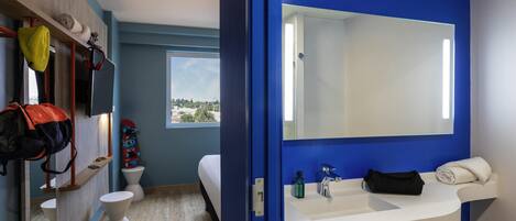 A modern bathroom with a blue accent wall, a large mirror, a white sink, and a toilet.