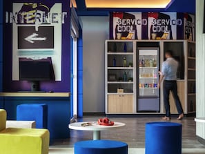 Un interior moderno con una computadora, un refrigerador para bebidas y asientos coloridos.