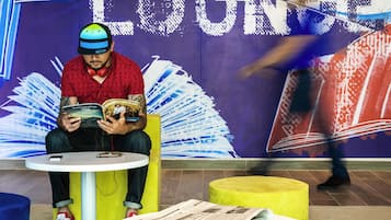A person sitting on a yellow chair in a room with a purple wall and the word 'LOUNGE' visible.