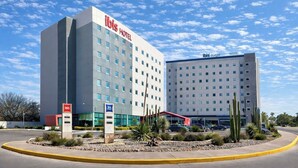 Un hotel moderno con un llamativo letrero que dice 'ibis Hotel', un segundo edificio identificado como 'ibis budget Hotel', y un estacionamiento con jardines de cactus.