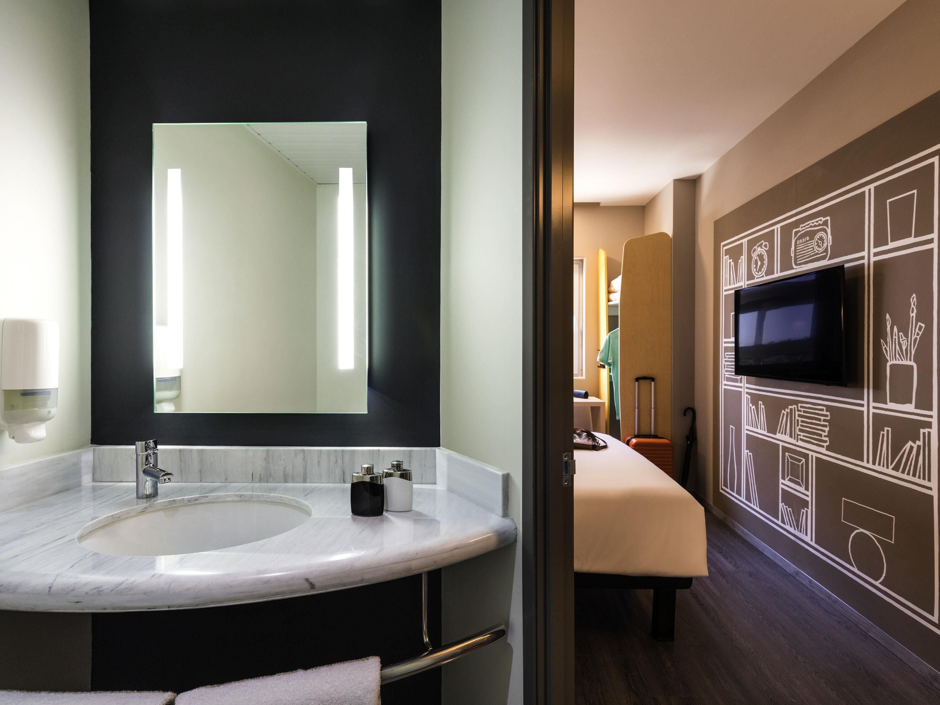 A modern bathroom with a large mirror, a sink, and a television mounted on the wall.
