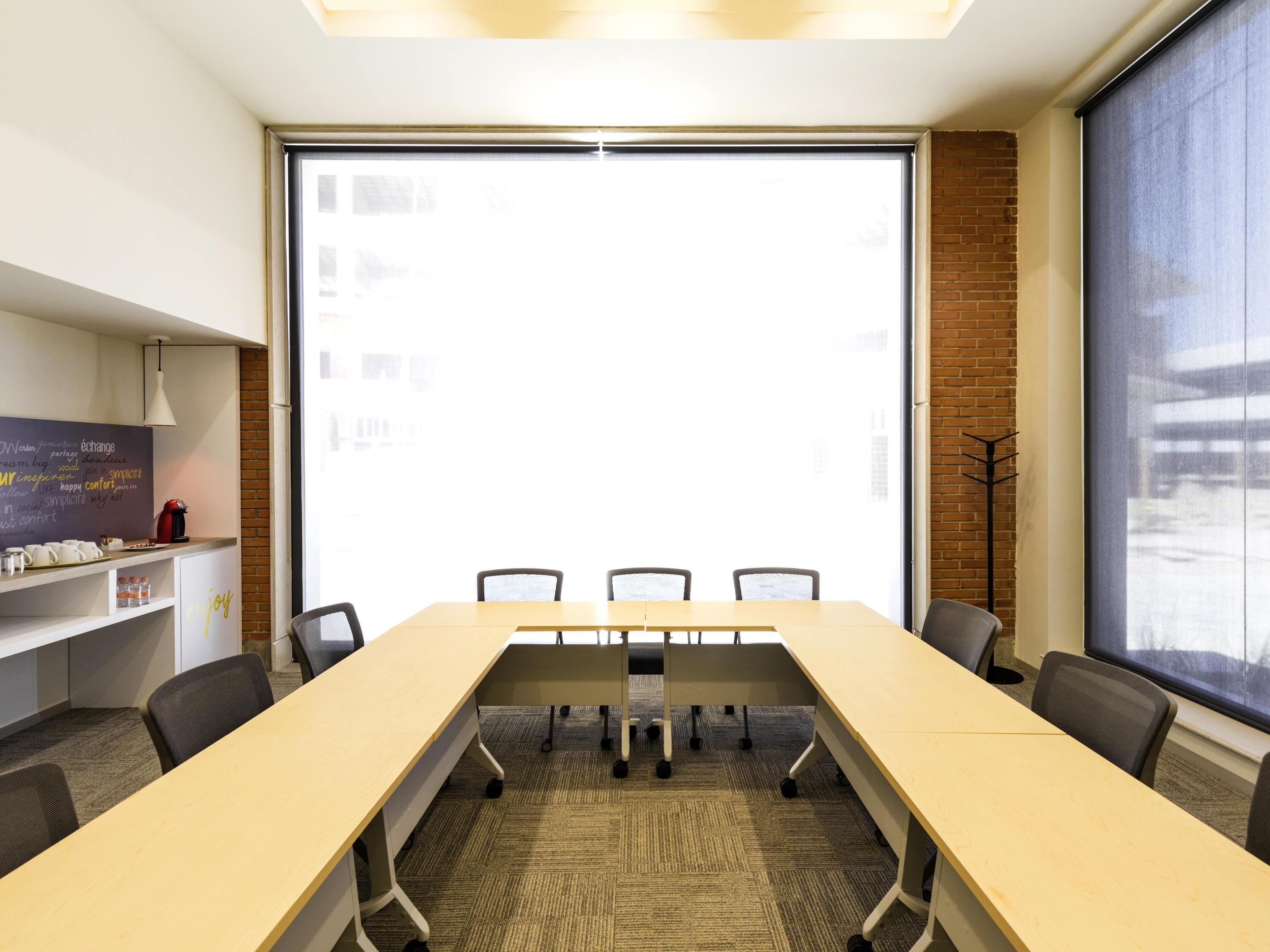 A conference room with a long table, chairs, a whiteboard, and a large window.