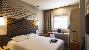 Una habitació d'hotel amb un llit gran, un escriptori amb un ordinador portàtil, una maleta i una finestra amb cortines.