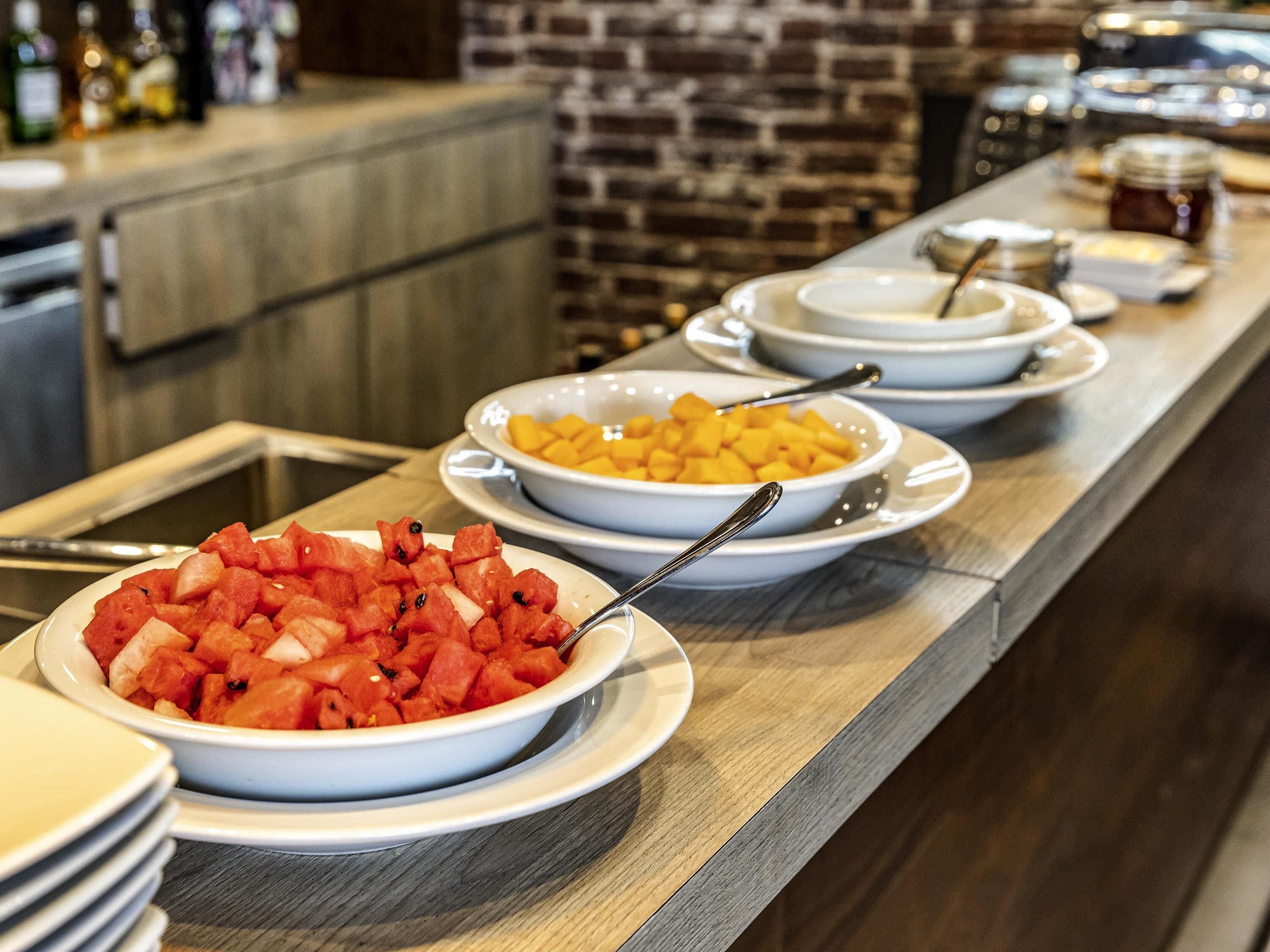 A buffet with various fruit dishes and a brick wall in the background.