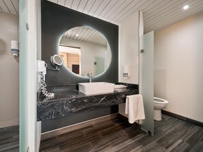 A modern bathroom with a black marble countertop, a white sink, a large mirror, and a toilet.