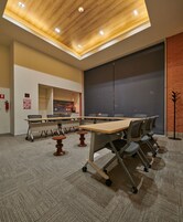 Sala de conferências com uma mesa grande, cadeiras, piso coberto de carpete, teto de madeira e parede de tijolos.