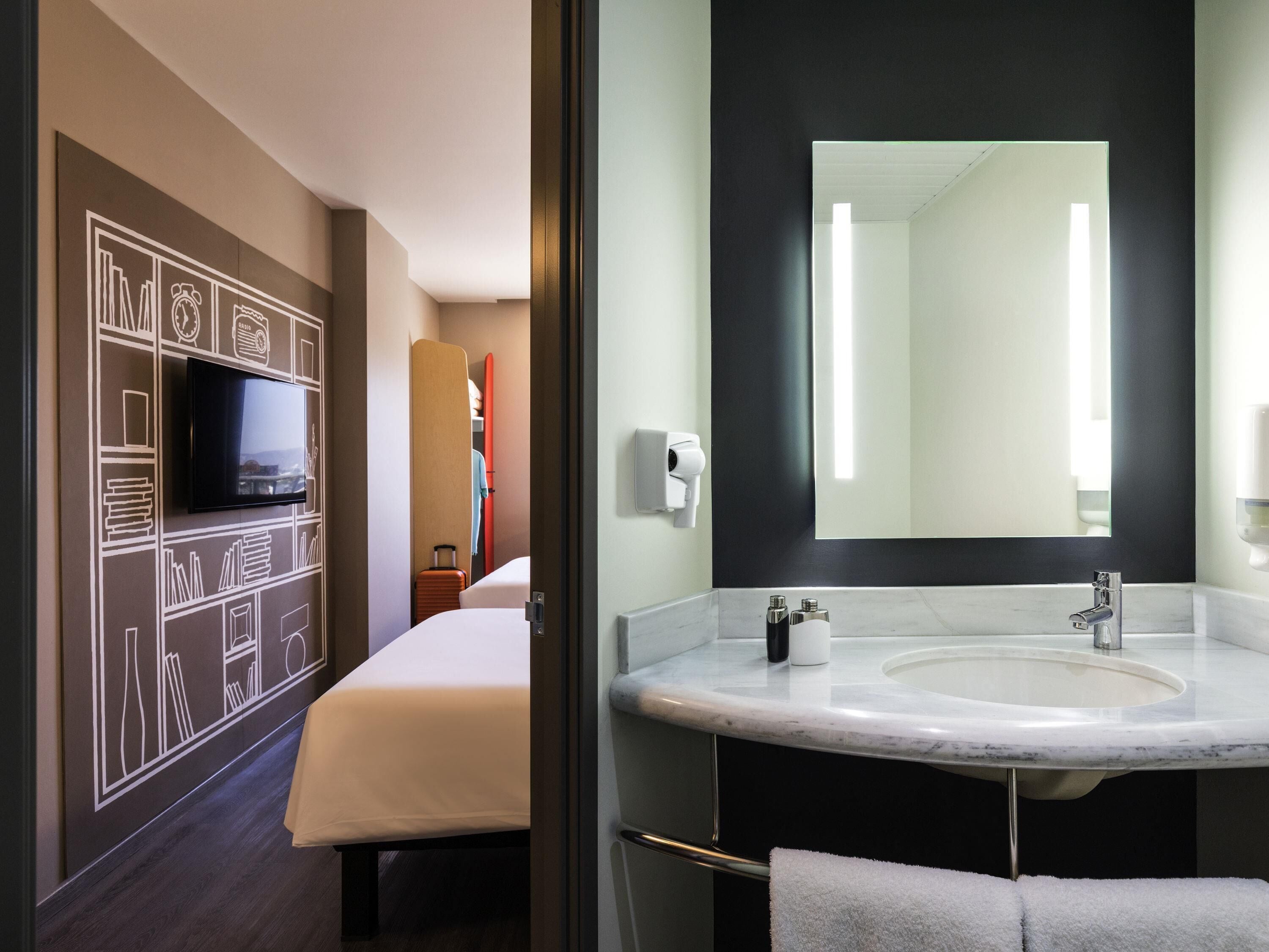 A hotel room with a bed, a television, a bathroom with a sink and mirror, and a towel rack.
