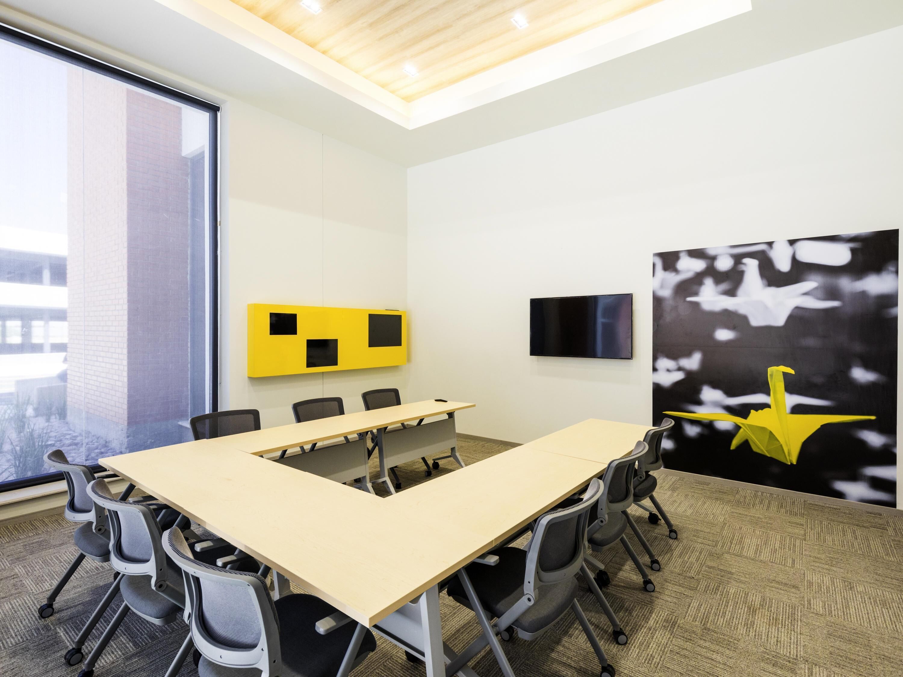 A conference room with a long table, chairs, a TV, and a large window.