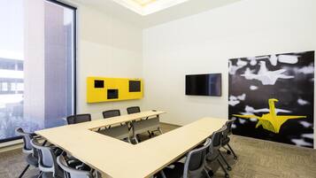 A conference room with a long table, chairs, a TV, and a large window.
