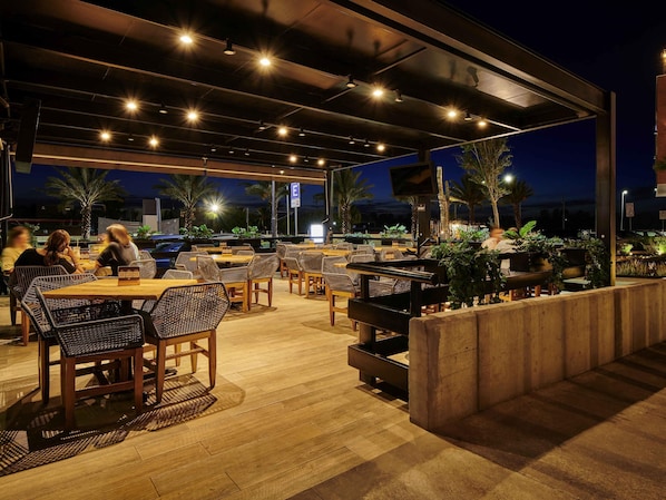An outdoor dining area with tables and chairs, a TV screen, and potted plants.