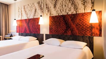 Habitación de hotel con dos camas, un cuadro abstracto grande en la pared y un escritorio con lámpara.
