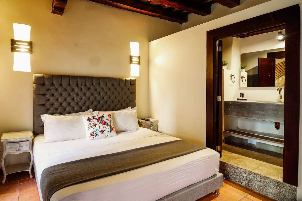 A neatly made bed with a tufted headboard, bedside tables, and wall-mounted lights.