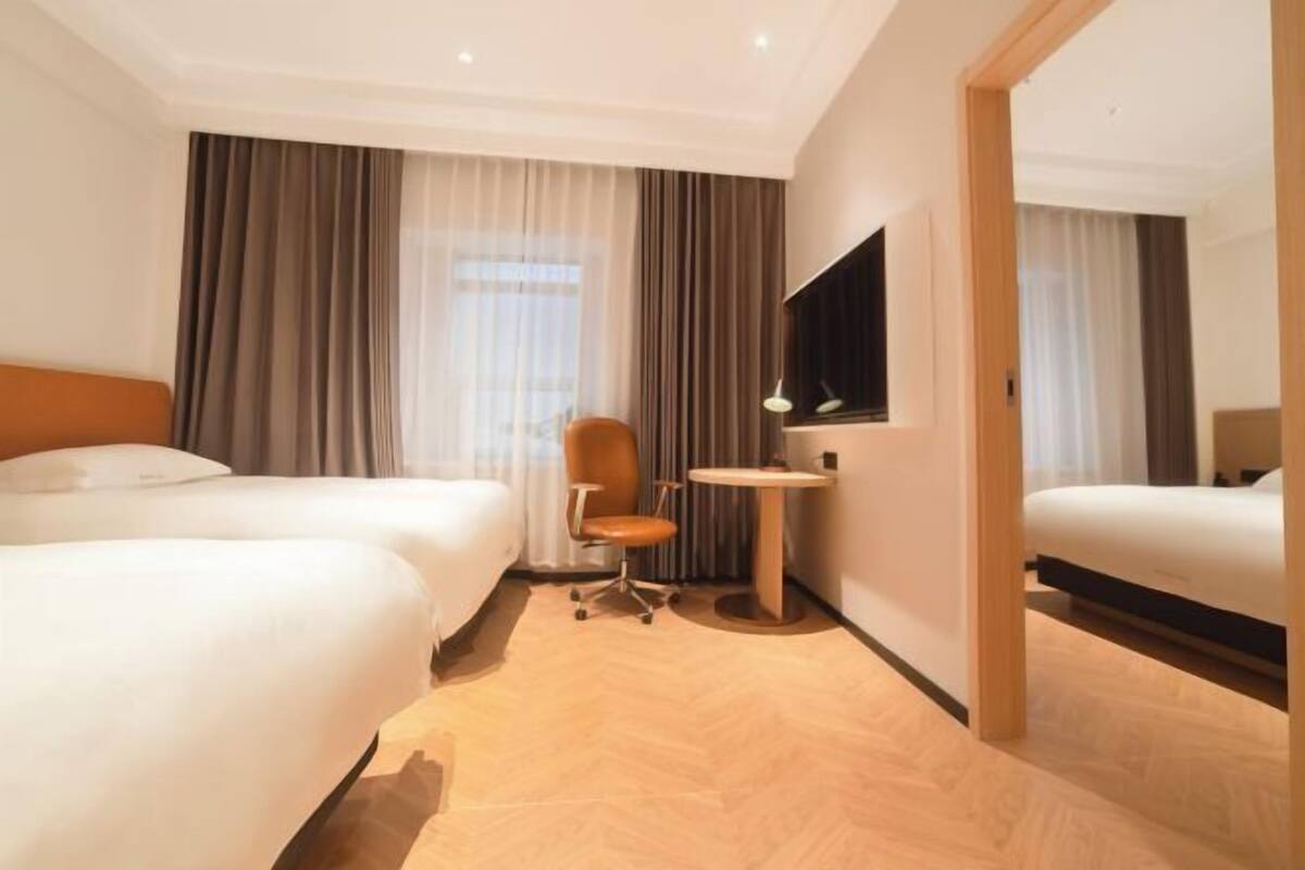 Ein Hotelzimmer mit zwei Betten, einem Schreibtisch, einem Stuhl und einem Fernseher.