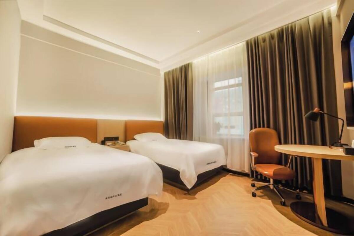 Ein Hotelzimmer mit zwei Betten, einem Schreibtisch, einem Stuhl und einem großen Fenster mit Vorhängen.