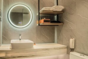 Ein Badezimmer mit rundem Spiegel, Waschbecken, Toilette und Handtuchhalter.