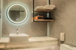 Un baño con un espejo redondo, un lavabo, un inodoro y un perchero para toallas.