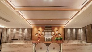A modern reception area with a marble reception desk, a decorative wall with geometric patterns, and a ceiling with recessed lighting. - Zhoucun Shaobing Hotel (Zibo)