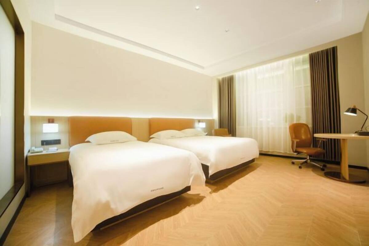 Ein Hotelzimmer mit zwei Betten, einem Schreibtisch, einem Stuhl und einer Lampe.