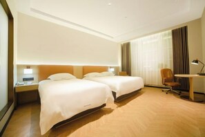 Ein Hotelzimmer mit zwei Betten, einem Schreibtisch, einem Stuhl und einer Lampe.