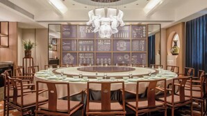 A round dining table with chairs, a chandelier, and a wall with framed artwork. - Zhoucun Shaobing Hotel (Zibo)