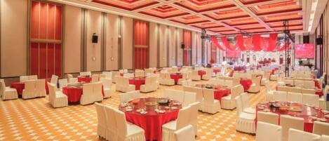 A banquet hall with round tables and chairs, a patterned floor, and a red and white color scheme.