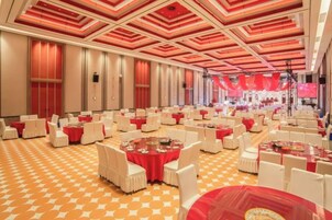 Un salón de banquetes con mesas y sillas redondas, piso estampado y decoración en tonos rojo y blanco.