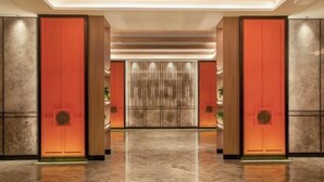 A modern hotel lobby with a polished marble floor, red accent walls, and a central decorative panel. - Zhoucun Shaobing Hotel (Zibo)