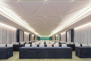 Un salón de conferencias con filas de mesas y sillas, un techo alto con diseños geométricos y una paleta de colores neutros.