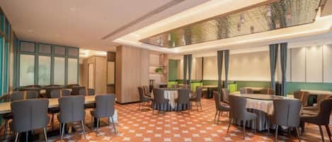 Comedor de hotel con varias mesas y sillas, piso estampado y un techo alto con iluminación empotrada.