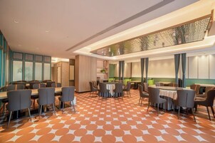 Comedor de hotel con varias mesas y sillas, piso estampado y un techo alto con iluminación empotrada.