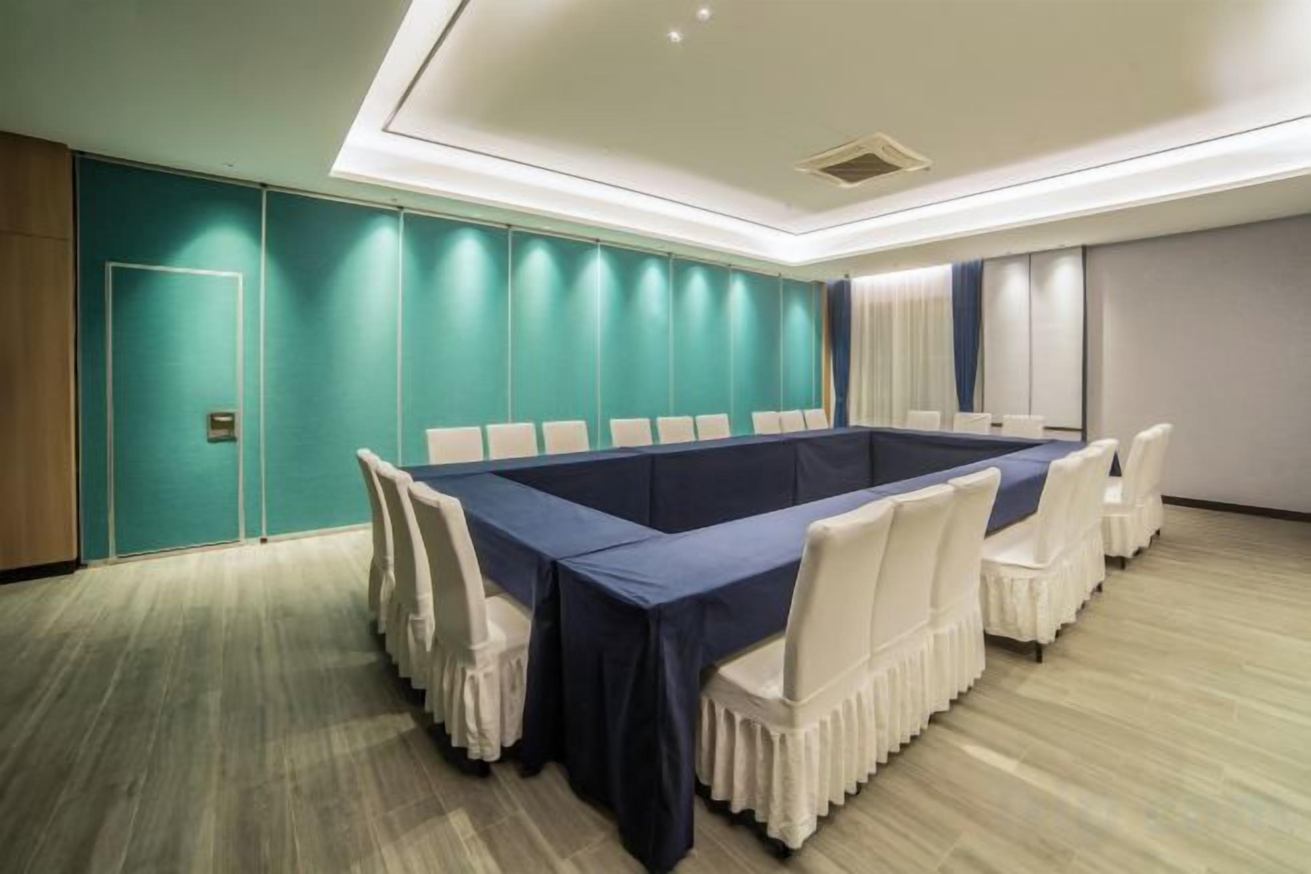 Une salle de conférence avec une longue table, des chaises blanches, des murs de couleur turquoise et un plancher en bois.